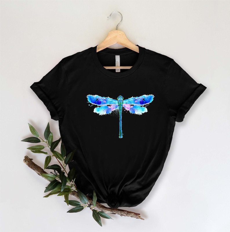 May include: Black t-shirt with a watercolor dragonfly design in shades of blue, pink, and purple.
