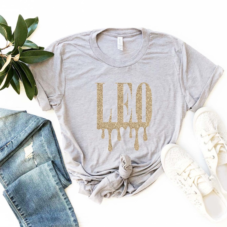 May include: A grey t-shirt with a gold glitter design that says "LEO" with drips coming from the letters.