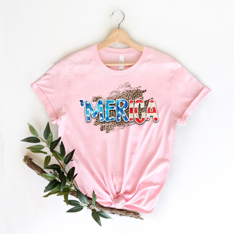 Op de afbeelding: Roze T-shirt met een verweerde, witte, rode en blauwe "'MERICA"-afbeelding op een luipaardprint.