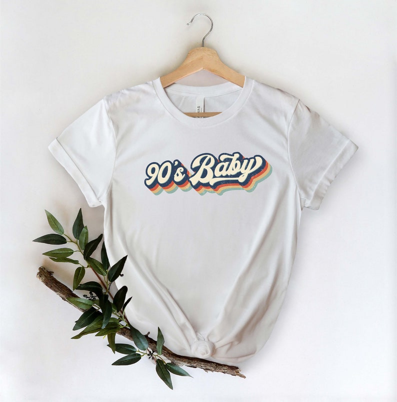 May include: White t-shirt with a retro-style graphic that says "90's Baby" in rainbow colors.