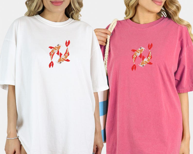 May include: White and pink t-shirts with a koi fish design. The koi fish are orange, white, and red. The t-shirts are oversized and have short sleeves. The white shirt is on the left, and the pink shirt is on the right.