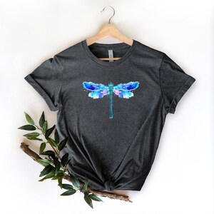 May include: A dark heather grey t-shirt with a watercolor dragonfly design in shades of blue, purple, and pink.