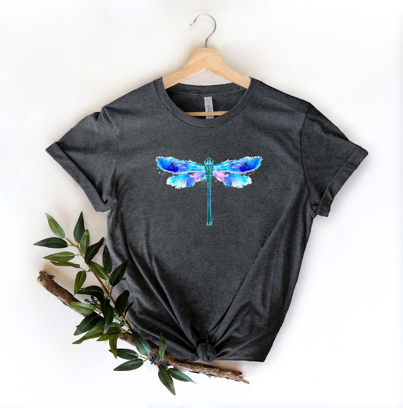 May include: A dark heather grey t-shirt with a watercolor dragonfly design in shades of blue, purple, and pink.
