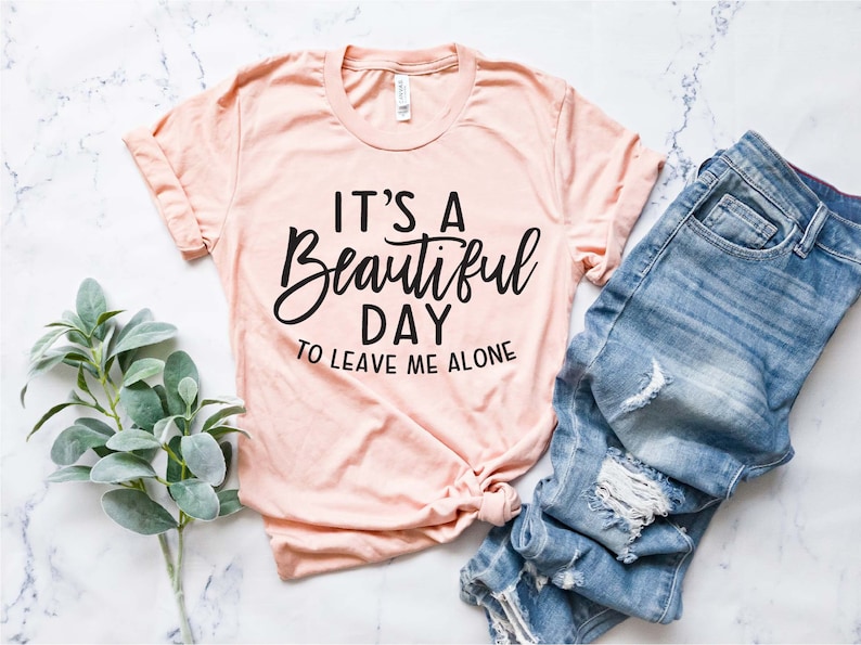 May include: A peach-colored t-shirt with black text that reads "It's a Beautiful Day to Leave Me Alone".