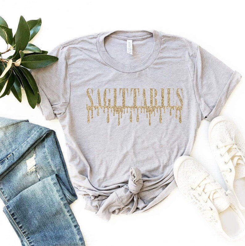 May include: A gray t-shirt with a gold glitter design that says "Sagittarius" with the letters dripping down.