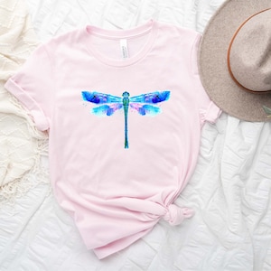 May include: A pink t-shirt with a watercolor dragonfly design in shades of blue, pink, and green.