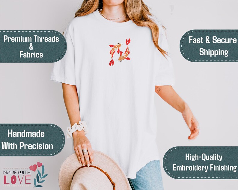 May include: White t-shirt with an embroidered design of two koi fish in shades of red and gold. The shirt features short sleeves and a relaxed fit. The image also includes text that says "Premium Threads & Fabrics", "Handmade With Precision", and "High-Quality Embroidery Finishing".
