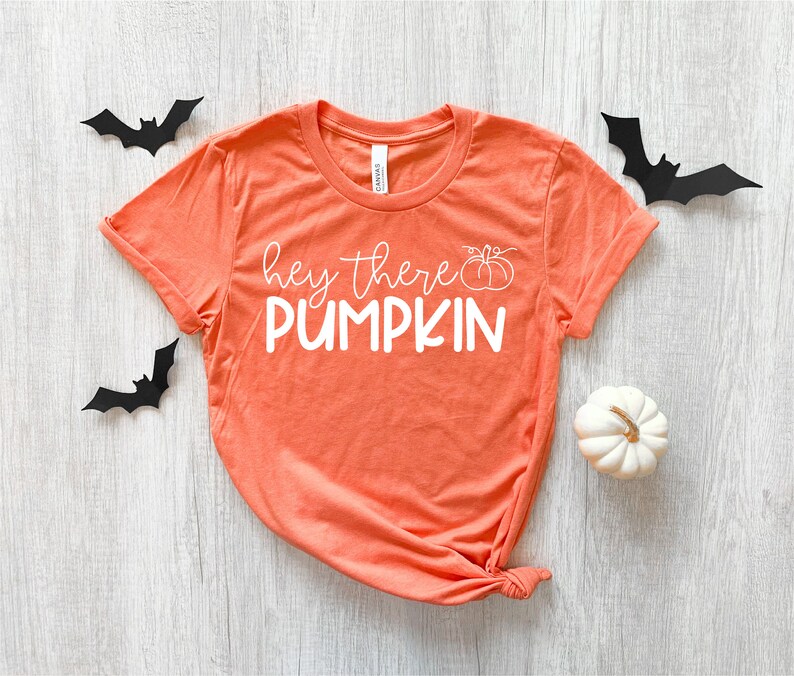 Puede incluir: Camiseta naranja de manga corta con el texto "hey there PUMPKIN" en blanco con un peque&ntilde;o gr&aacute;fico de calabaza.