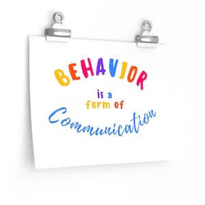 May include: A white poster with the text "BEHAVIOR is a form of COMMUNICATION" in rainbow colors. The poster is hanging on a white wall with two silver clips.