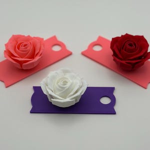May include: Three paper roses, one pink, one white, and one red, are displayed on colorful paper tags. The tags have a hole punched in the top.