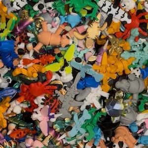 May include: A vibrant assortment of colorful, miniature figurines. The collection includes various animal shapes like frogs, crabs, and bears, along with other whimsical designs. The figurines are in shades of green, orange, blue, and white, creating a playful and diverse display.