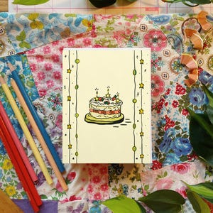 Puede incluir: Una tarjeta de felicitación de cumpleaños con un fondo amarillo, que presenta una ilustración de pastel con velas. La tarjeta está decorada con líneas verticales de círculos verdes y estrellas amarillas. Se ven lápices de colores y una regla de madera.