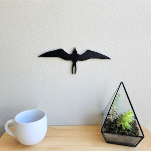 Può includere: Decorazione da parete in legno nero a forma di silhouette di uccello con un terrario di vetro con piante verdi su una superficie di legno.
