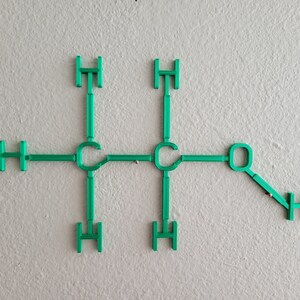 May include: A green model of a chemical molecule with the letters C, H, and O. The molecule is made of plastic and is attached to a white wall.