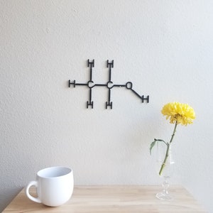 May include: A black metal wall decor in the shape of a chemical structure with a single yellow flower in a clear glass vase on a wooden table.