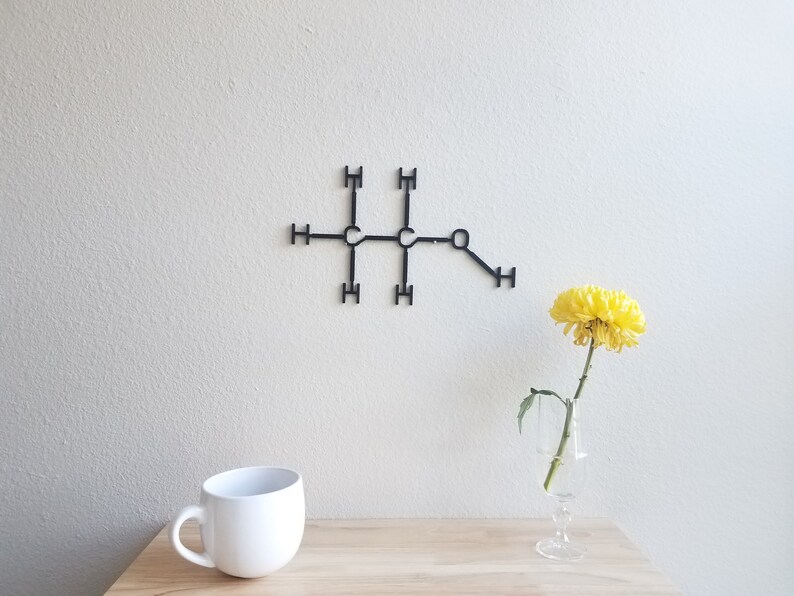 May include: A black metal wall decor in the shape of a chemical structure with a single yellow flower in a clear glass vase on a wooden table.