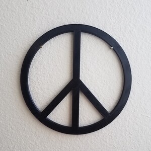 May include: A black peace sign wall decor with a simple design. The peace sign is made of a thick, solid material and has a smooth, glossy finish.