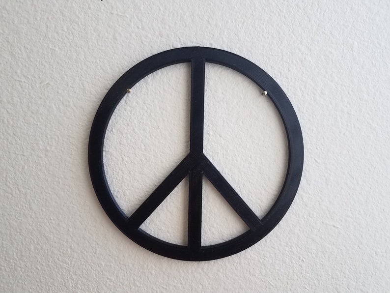 May include: A black peace sign wall decor with a simple design. The peace sign is made of a thick, solid material and has a smooth, glossy finish.
