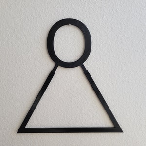 K&ouml;nnte beinhalten: Schwarze Wanddekoration aus Metall in Form eines Kreises mit einem Dreieck darunter.