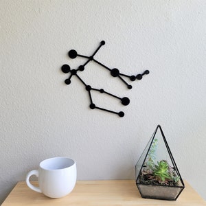 May include: Black metal wall decor in the shape of the Gemini constellation. The decor is made of thin metal and features a series of connected circles.