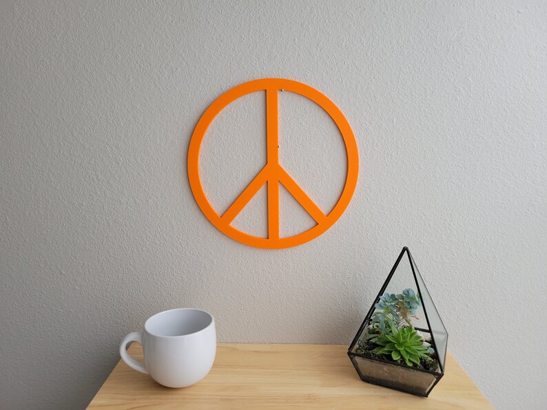 May include: Orange peace sign wall decor with a white mug and a glass terrarium with a succulent plant on a wooden surface.