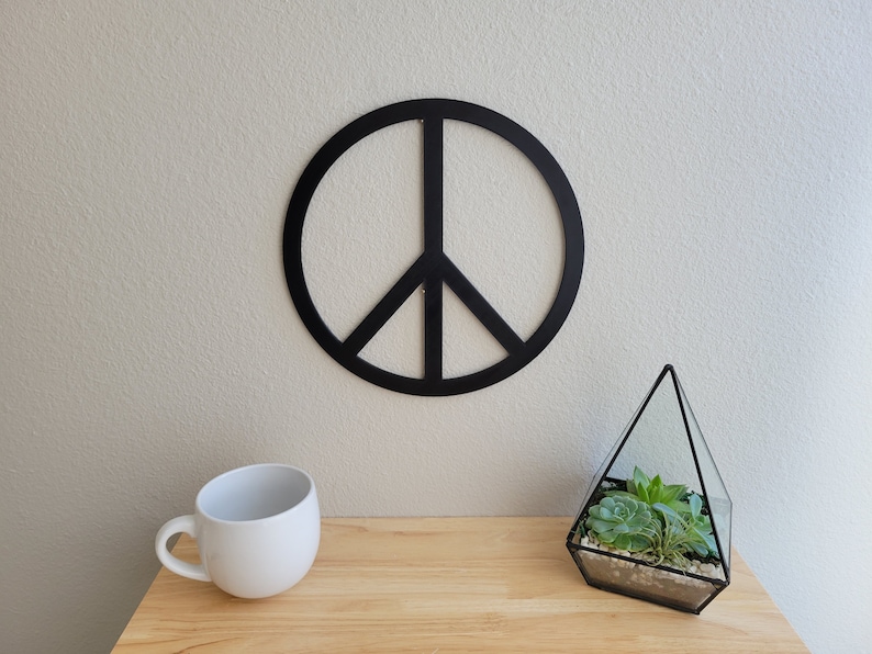 May include: Black peace sign wall decor with a glass terrarium filled with succulents on a wooden surface.