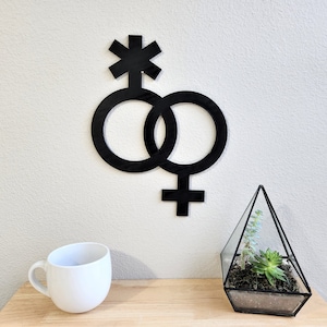 May include: Black wooden wall decor featuring two interlocking circles with a four-pointed star at the top. The circles are connected by a cross shape.