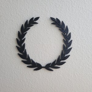 K&ouml;nnte beinhalten: Ein schwarzer Lorbeerkranz auf einer wei&szlig;en Wand.