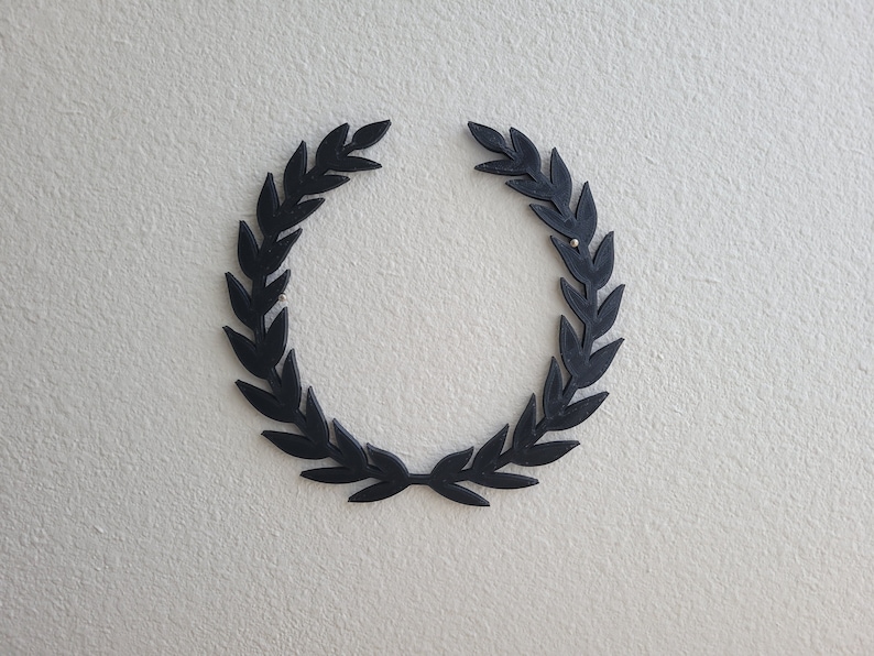 K&ouml;nnte beinhalten: Ein schwarzer Lorbeerkranz auf einer wei&szlig;en Wand.