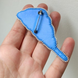 May include: The back of a blue beaded brooch with a silver pin and clasp.