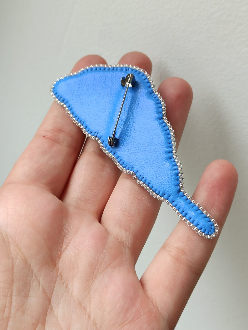 May include: The back of a blue beaded brooch with a silver pin and clasp.