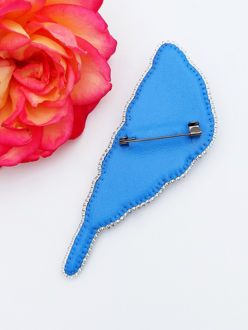 May include: Blue beaded bird brooch with a silver pin on the back. The brooch is shaped like a bird with a long tail.