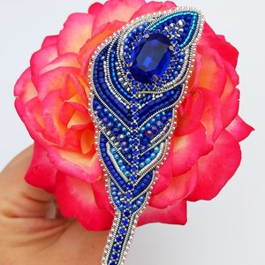 May include: A blue and silver beaded feather brooch with a large blue rhinestone in the center.