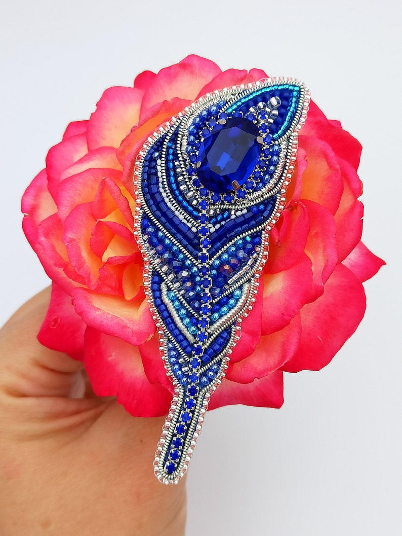 May include: A blue and silver beaded feather brooch with a large blue rhinestone in the center.