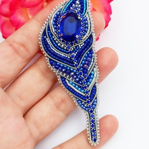 May include: A blue and silver beaded feather brooch with a large blue rhinestone in the center.