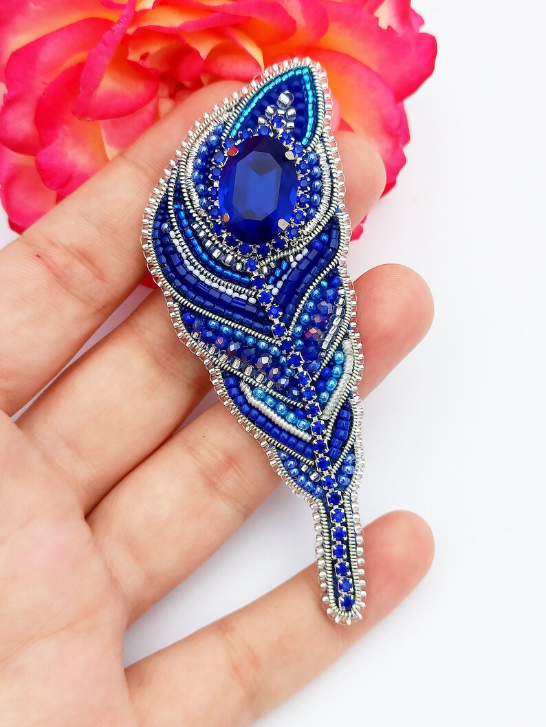 May include: A blue and silver beaded feather brooch with a large blue rhinestone in the center.