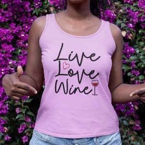May include: A pink tank top with the text "Live Love Wine" in black script. A small red heart is above the word "Love" and a glass of red wine is next to the word "Wine".