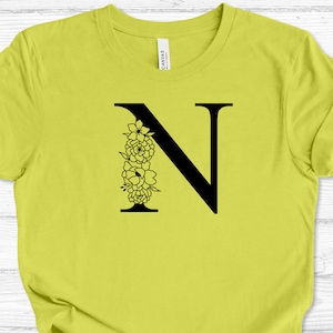 May include: A yellow t-shirt with a black floral letter N design.