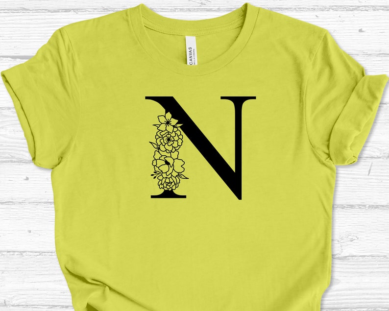 May include: A yellow t-shirt with a black floral letter N design.