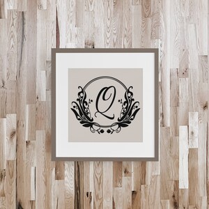 May include: A framed print with a black and white design of a stylized letter Q surrounded by floral elements. The letter Q is inside a circle and the floral elements are on the outside of the circle. The background of the print is a light beige color.