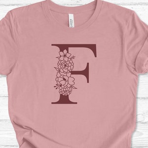 May include: A pink t-shirt with a burgundy floral letter F design.