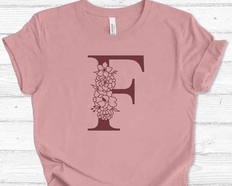 May include: A pink t-shirt with a burgundy floral letter F design.