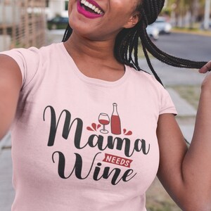 May include: Pink t-shirt with the text "Mama Needs Wine" in black cursive font. A glass of wine and a bottle of wine are depicted in red.