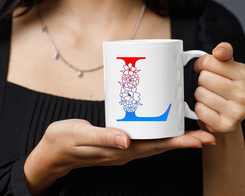 May include: White ceramic mug with a blue and red floral design featuring the letter L. The mug has a handle.