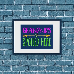 May include: A framed print with a blue background and the text "Grandkids Spoiled Here" in green, pink, and gold lettering. An arrow with a heart is above the text.