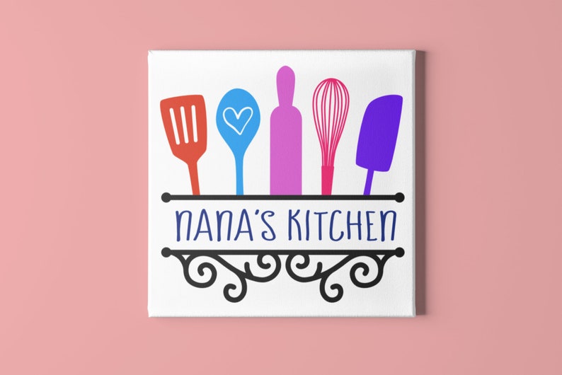 May include: A white canvas with a black sign that says "NANA'S KITCHEN".  The sign has a decorative scroll design and is hanging from a black rod.  There are five colorful kitchen utensils hanging from the rod: a red spatula, a blue spoon with a white heart, a pink rolling pin, a pink whisk, and a purple spatula.