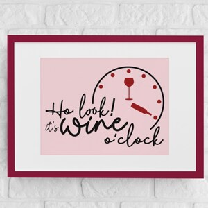 May include: A pink framed print with a black and white clock face with a wine glass and bottle on it. The text reads "Ho look! It's wine o'clock".