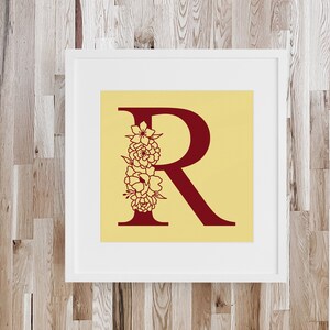 May include: A framed print with a yellow background and a red letter "R" with a floral design. The floral design is in the shape of a bouquet of flowers.