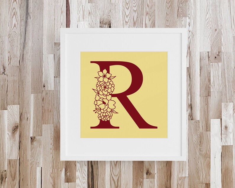 May include: A framed print with a yellow background and a red letter "R" with a floral design. The floral design is in the shape of a bouquet of flowers.