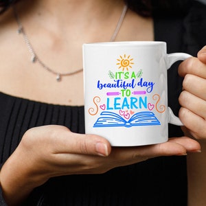 May include: White ceramic mug with a colorful design that says "It's a beautiful day to learn" with a sun, book, and hearts.